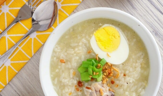 Chicken Arroz Caldo in white serving bowls topped with boiled egg, green onions, and fried garlic bits