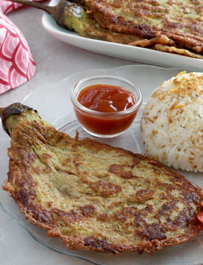 eggplant omelette on a plate with steamed rice and ketchup.